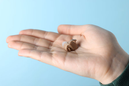 Woman with hearing aid on light blue background, closeup