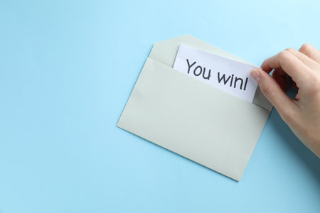 Woman taking card with text You Win! from envelope on light blue background, top view. Space for textの写真素材