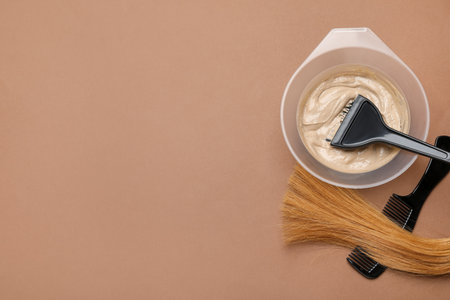 Hair dye in bowl, brush, lock of hair and comb on brown background, flat lay. Space for textの写真素材