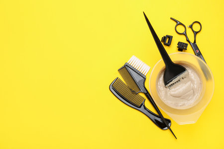 Hair dye in bowl and hairdresser's tools on yellow background, flat lay. Space for textの写真素材