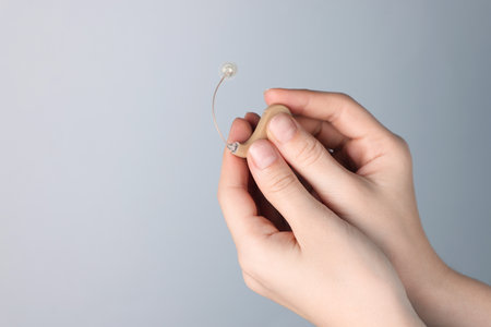 Woman with hearing aid on light gray background, closeup. Space for textの写真素材