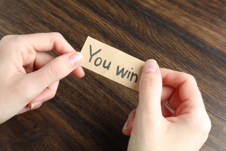 Woman holding paper note with text You Win at wooden table, closeupの写真素材
