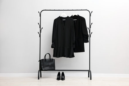 Different stylish clothes hanging on rack, bag and shoes near light wall indoorsの写真素材