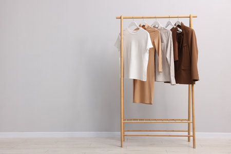 Different stylish clothes hanging on rack near light wall indoors, space for textの写真素材