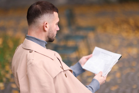 Young man reading newspaper outdoors. Space for textの写真素材