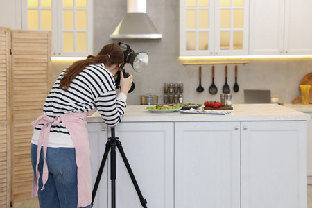 Woman taking picture of meal at table in kitchen.の写真素材
