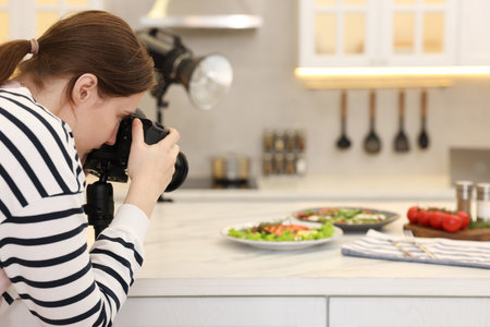 Woman taking picture of meal at table in kitchen. Professional food photographyの写真素材