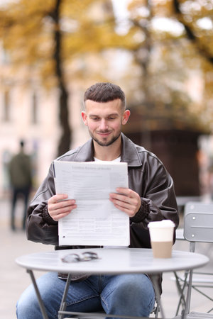 Young man reading newspaper at table in outdoor cafe
