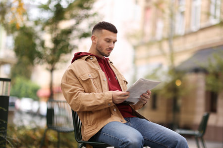 Young man reading newspaper on chair outdoorsの写真素材