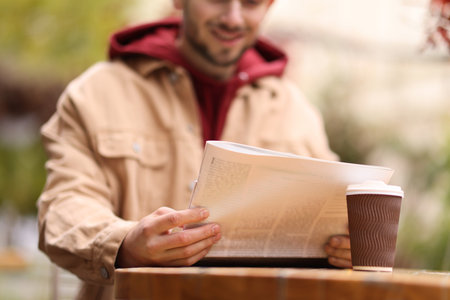 Young man reading newspaper at table in outdoor cafe, closeupの写真素材