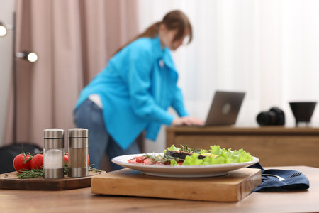 Tasty salmon with vegetables on wooden table and woman looking at pictures on laptop after shooting in studio, selective focus. Food photographyの写真素材