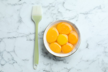 Egg yolks in bowl and brush on white marble table, flat layの写真素材