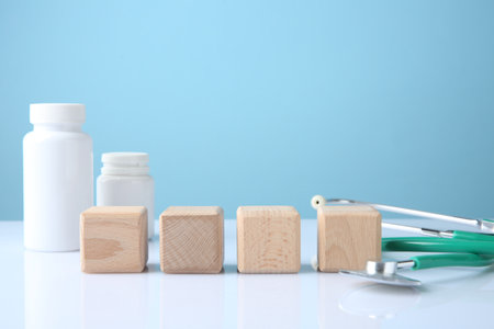 Stethoscope, pills and blank wooden cubes on white table against light blue background. Mockup for designの写真素材