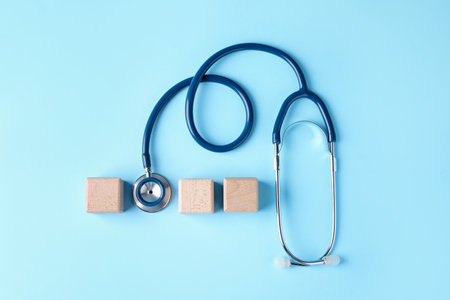 Stethoscope and blank wooden cubes on light blue background, flat lay. Mockup for designの写真素材