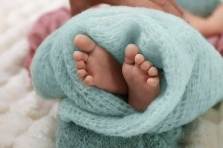 Newborn baby wrapped in knitted blanket lying on bed, closeupの写真素材