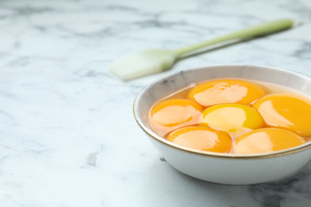 Egg yolks in bowl and brush on white marble table, closeup. Space for textの写真素材