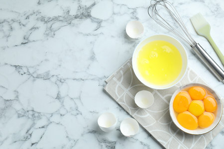 Egg whites, yolks, whisk and brush on white marble table, flat lay. Space for textの写真素材