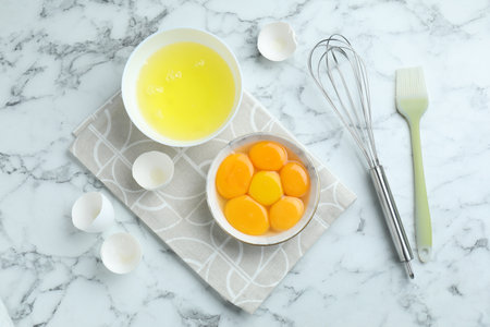 Egg whites, yolks, whisk and brush on white marble table, flat layの写真素材