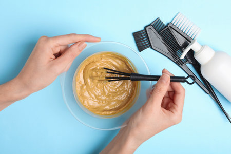 Woman mixing hair dye in bowl and tools on light blue background, top viewの写真素材