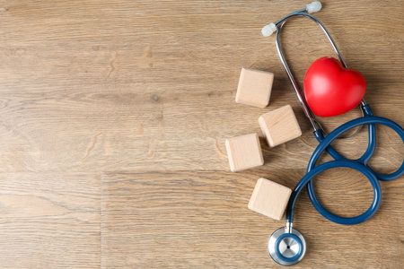 Stethoscope, heart figure and blank cubes on wooden background, flat lay. Mockup for designの写真素材