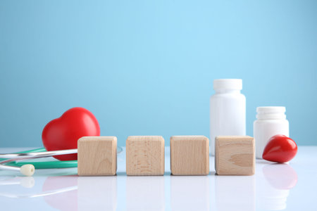 Stethoscope, pills, heart figures and blank wooden cubes on white table against light blue background. Mockup for designの写真素材