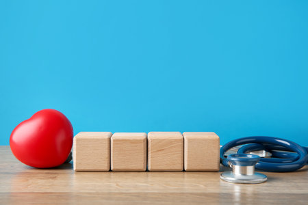 Stethoscope, heart figure and blank cubes on wooden table against light blue background. Mockup for designの写真素材