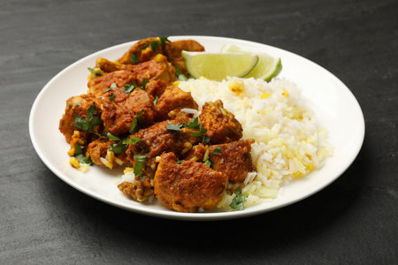 Delicious chicken tikka masala with rice, parsley and lime on dark textured table, closeupの写真素材