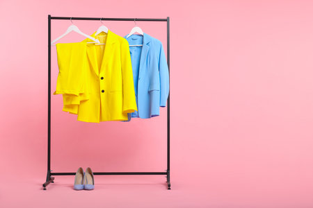 Different clothes hanging on rack and shoes against pink background, space for textの写真素材