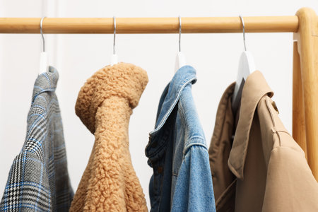 Different stylish clothes hanging on rack near white wall indoors, closeupの写真素材