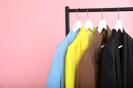 Different clothes hanging on rack against pink background, closeup. Space for textの写真素材