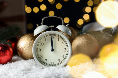 New Year celebration. Alarm clock and festive decor on artificial snow against blurred lights, closeupの写真素材