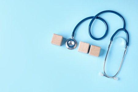 Stethoscope and blank wooden cubes on light blue background, flat lay. Mockup for designの写真素材
