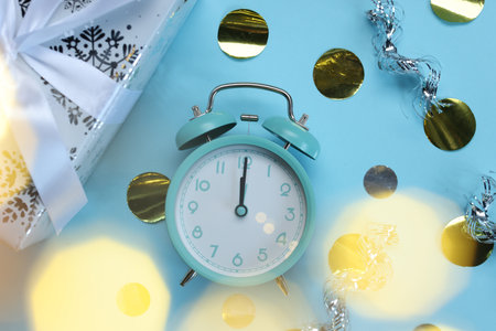 New Year celebration. Alarm clock and festive decor on light blue background, flat layの写真素材