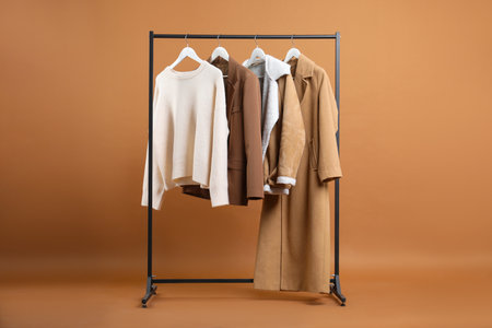 Different clothes hanging on rack against brown backgroundの写真素材