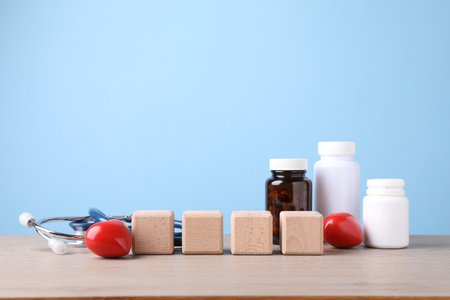 Stethoscope, pills, heart figures and blank cubes on wooden table against light blue background. Mockup for designの写真素材