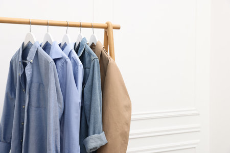 Different stylish clothes hanging on rack near white wall indoors. Space for textの写真素材