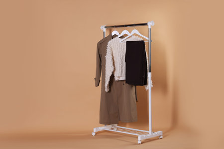 Different stylish clothes hanging on rack against beige background, space for text