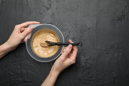 Woman mixing substance in bowl on black textured background, top view. Space for textの写真素材