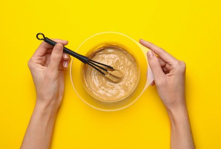 Woman mixing substance in bowl on yellow background, top viewの写真素材
