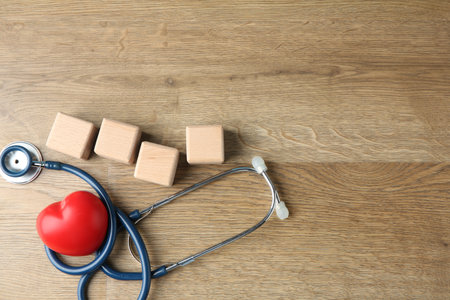 Stethoscope, heart figure and blank cubes on wooden background, flat lay. Mockup for designの写真素材