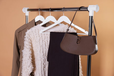 Different stylish clothes and bag hanging on rack against beige background, closeupの写真素材