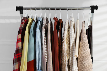 Different stylish clothes hanging on rack near white wall indoors, closeupの写真素材