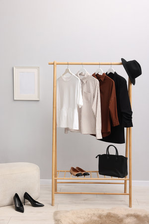 Different stylish clothes hanging on rack, bag and shoes near light wall indoorsの写真素材