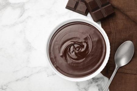 Melted chocolate in bowl, pieces and spoon on white marble table, flat lay. Space for textの写真素材