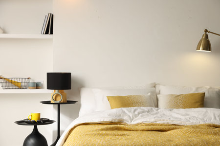 Large bed with linens, bedside tables and lamp near white wall in bedroomの写真素材