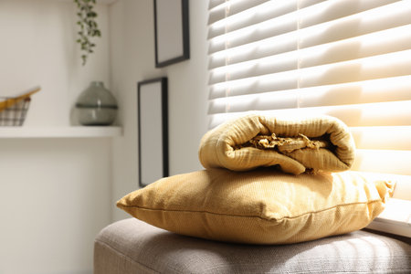 Soft pillow and blanket on pouf near window, closeup. Space for textの写真素材