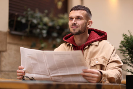Young man reading newspaper at table in outdoor cafe