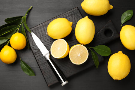 Fresh lemons with green leaves and knife on black wooden table, flat layの写真素材