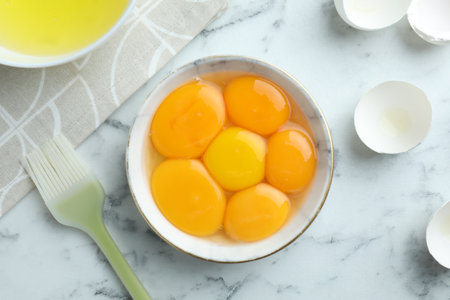 Egg yolks, whites and brush on white marble table, flat layの写真素材