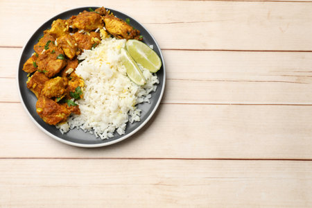 Delicious chicken tikka masala with rice, parsley and lime on light wooden table, top view. Space for textの写真素材